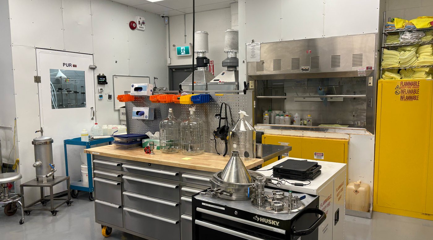 The Protonify processing room — fume hood, flammables cabinets, glassware and tool chests, with the purification room visible through a window